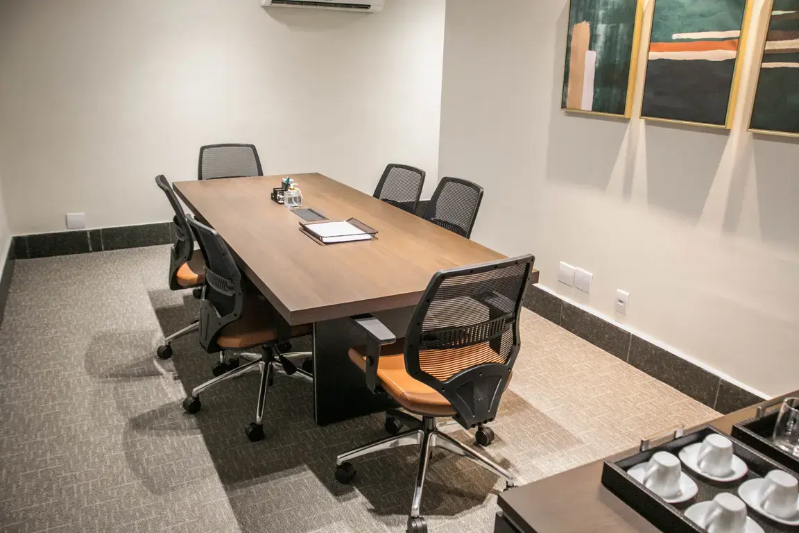 Sala de reunião com mesa, cadeiras de escritório e piso.